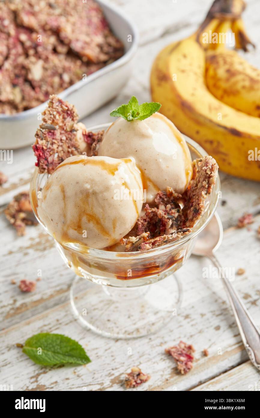 Cucchiai di bella crema di banana condita con salsa al caramello e briciole di biscotti: Un dessert surgelato vegano, dolce e cremoso, perfetto per l'estate. Foto Stock