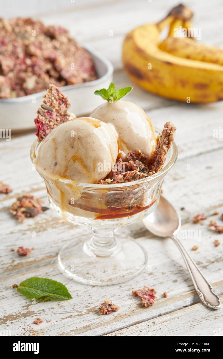 Cucchiai di bella crema di banana condita con salsa al caramello e briciole di biscotti: Un dessert surgelato vegano, dolce e cremoso, perfetto per l'estate. Foto Stock
