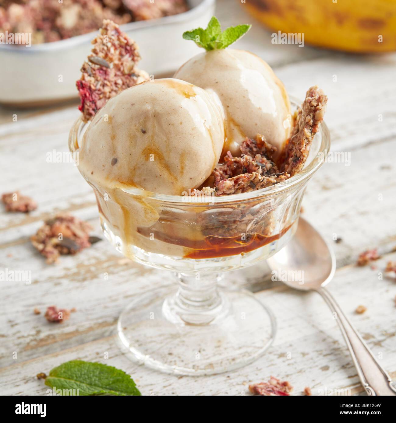 Cucchiai di bella crema di banana condita con salsa al caramello e briciole di biscotti: Un dessert surgelato vegano, dolce e cremoso, perfetto per l'estate. Foto Stock