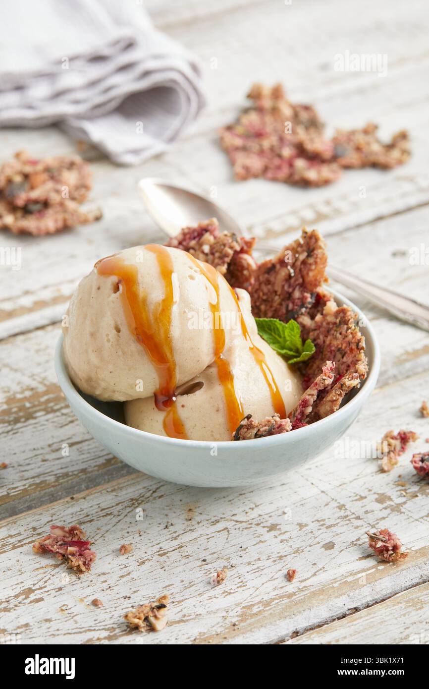 Cucchiai di bella crema di banana condita con salsa al caramello e briciole di biscotti: Un dessert surgelato vegano, dolce e cremoso, perfetto per l'estate. Foto Stock