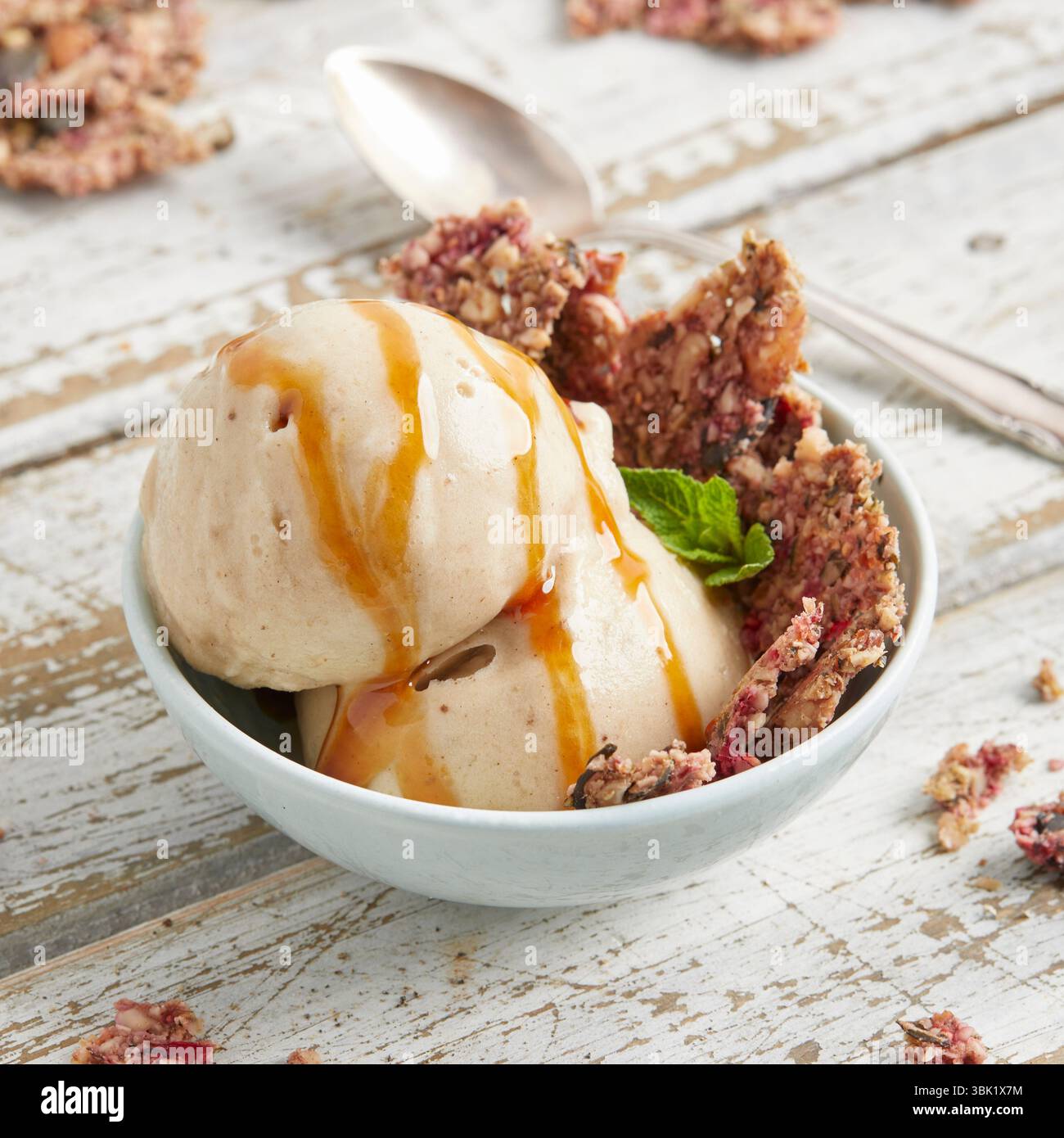 Cucchiai di bella crema di banana condita con salsa al caramello e briciole di biscotti: Un dessert surgelato vegano, dolce e cremoso, perfetto per l'estate. Foto Stock