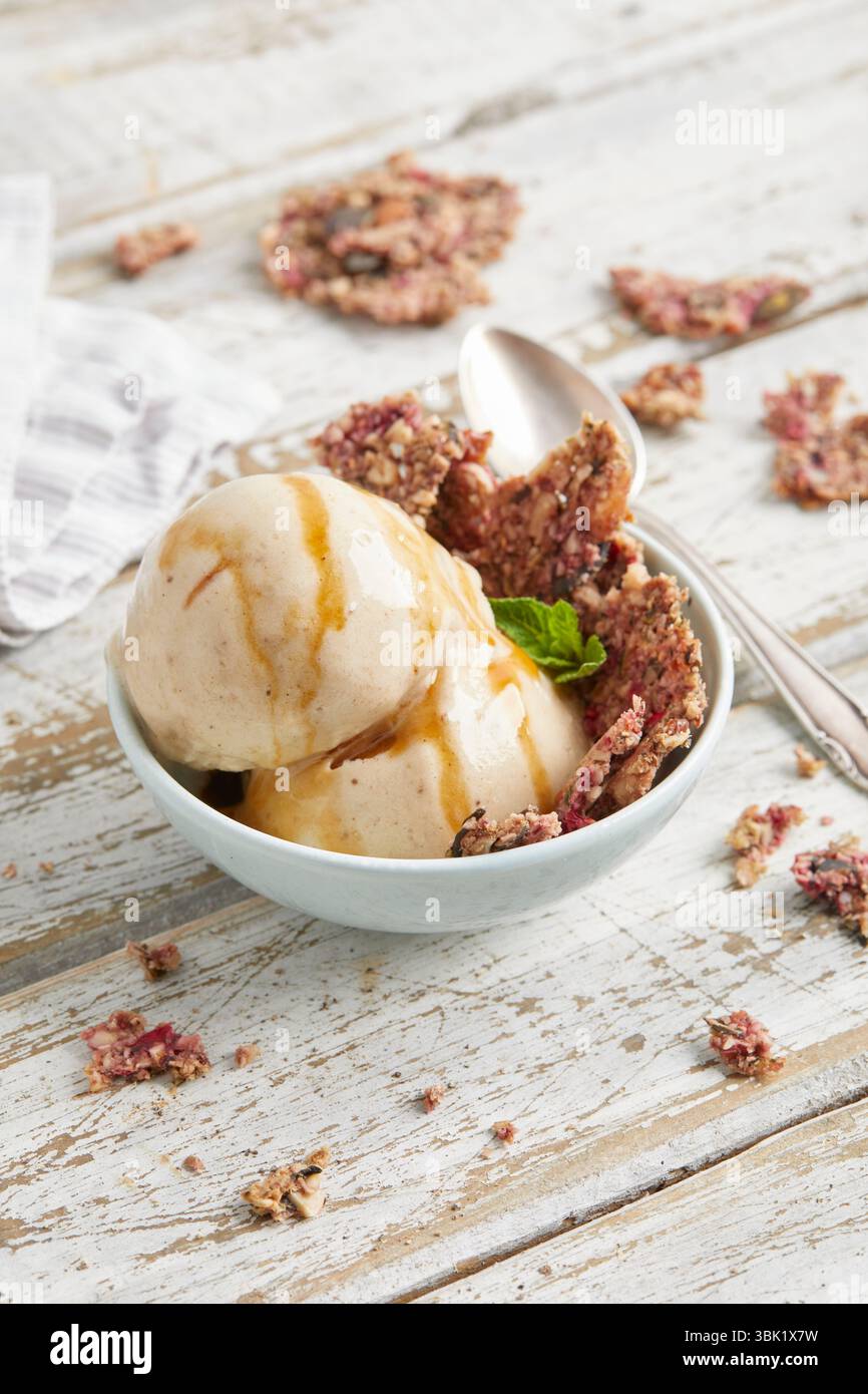 Cucchiai di bella crema di banana condita con salsa al caramello e briciole di biscotti: Un dessert surgelato vegano, dolce e cremoso, perfetto per l'estate. Foto Stock