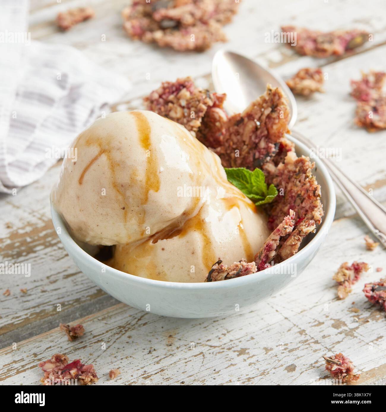 Cucchiai di bella crema di banana condita con salsa al caramello e briciole di biscotti: Un dessert surgelato vegano, dolce e cremoso, perfetto per l'estate. Foto Stock