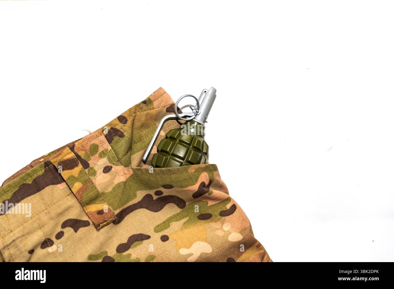 Granata a mano in plastica finta posta nella tasca di pantaloni camouflage in stile militare. Immagine simbolica di guerra, pericolo o addestramento militare. Uso editoriale Foto Stock