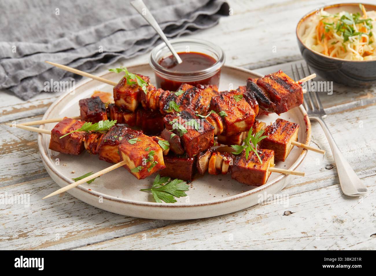 Spiedini di tofu con salsa da immersione su un piatto, serviti con insalata di cavolo croccante in una piccola ciotola: Un pasto abbondante a base di piante, ideale per pranzo o cena. Foto Stock