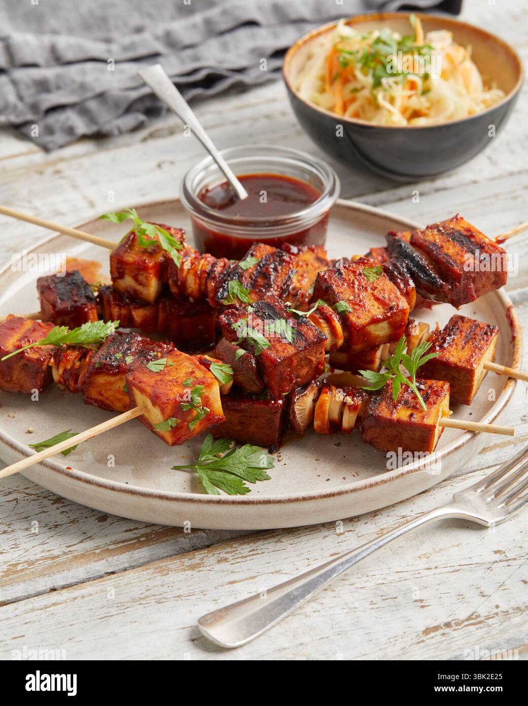 Spiedini di tofu con salsa da immersione su un piatto, serviti con insalata di cavolo croccante in una piccola ciotola: Un pasto abbondante a base di piante, ideale per pranzo o cena. Foto Stock