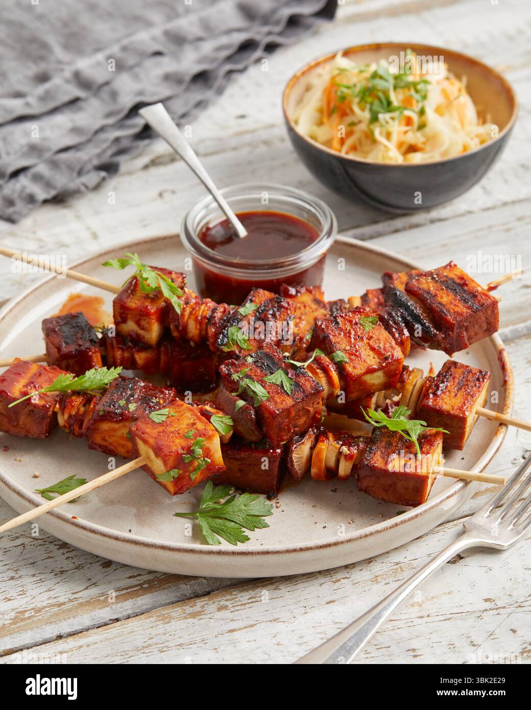 Spiedini di tofu con salsa da immersione su un piatto, serviti con insalata di cavolo croccante in una piccola ciotola: Un pasto abbondante a base di piante, ideale per pranzo o cena. Foto Stock
