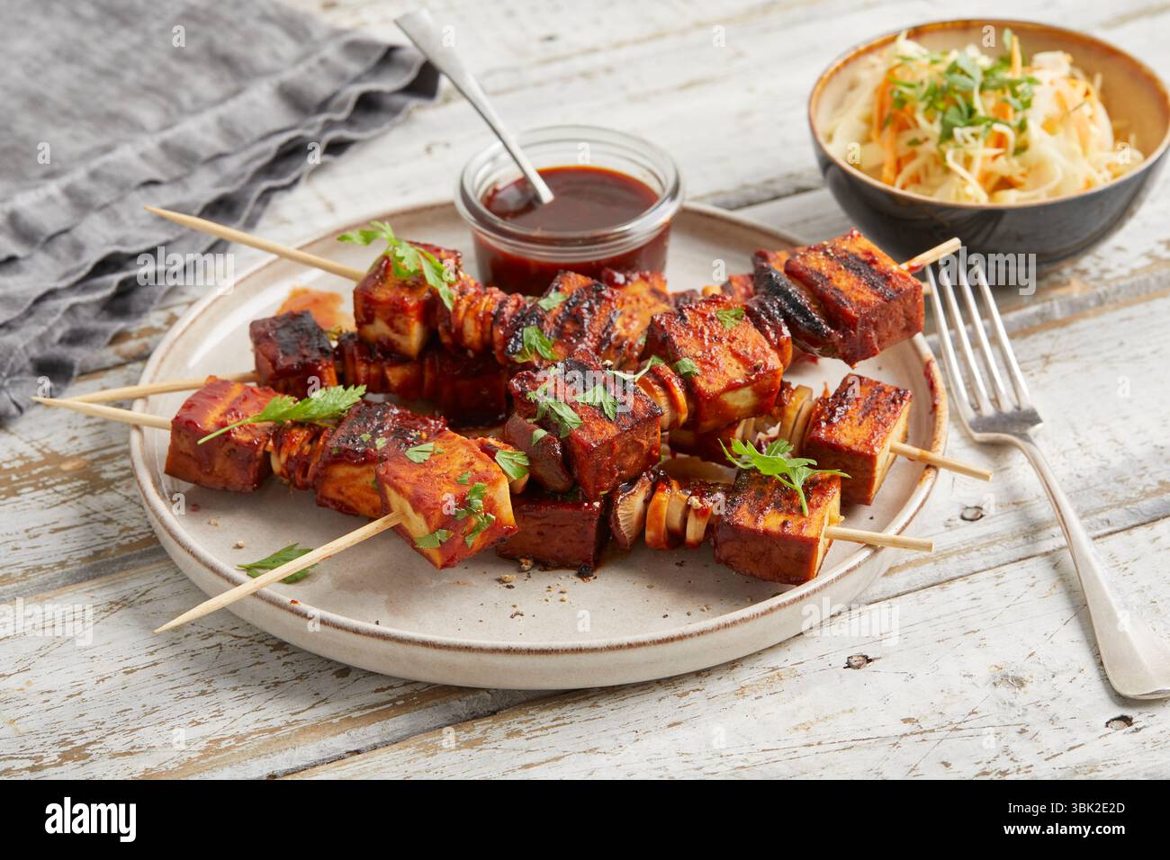 Spiedini di tofu con salsa da immersione su un piatto, serviti con insalata di cavolo croccante in una piccola ciotola: Un pasto abbondante a base di piante, ideale per pranzo o cena. Foto Stock