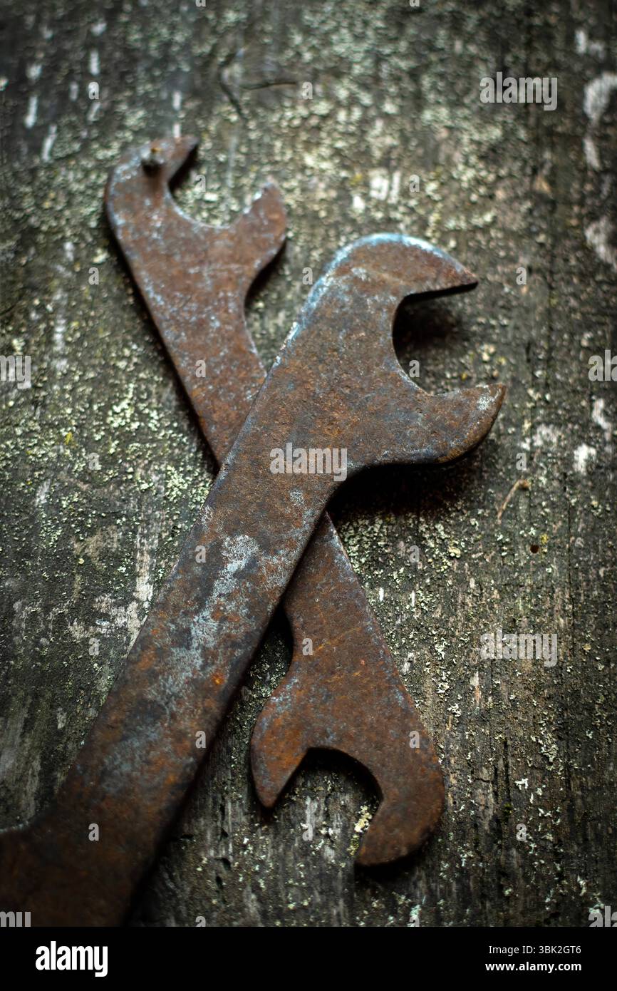Due vecchie chiavi poggiano incrociate su una superficie di legno intemprata, rivelando la loro ruggine e segni di molti anni di lavoro meccanico Foto Stock