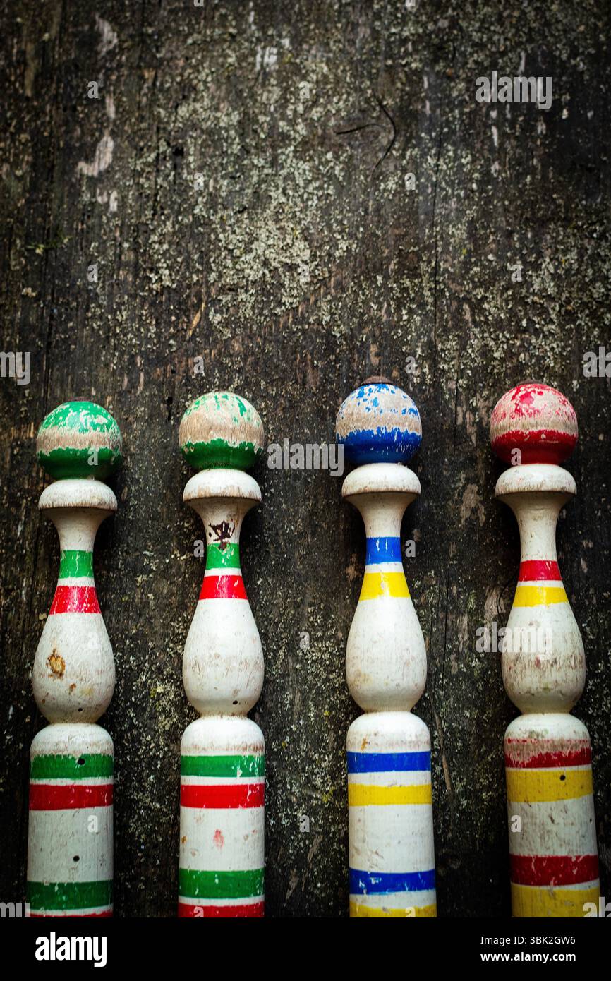 Quattro birilli da bowling in legno vintage dai colori vivaci si trovano in fila su una superficie rustica in legno Foto Stock