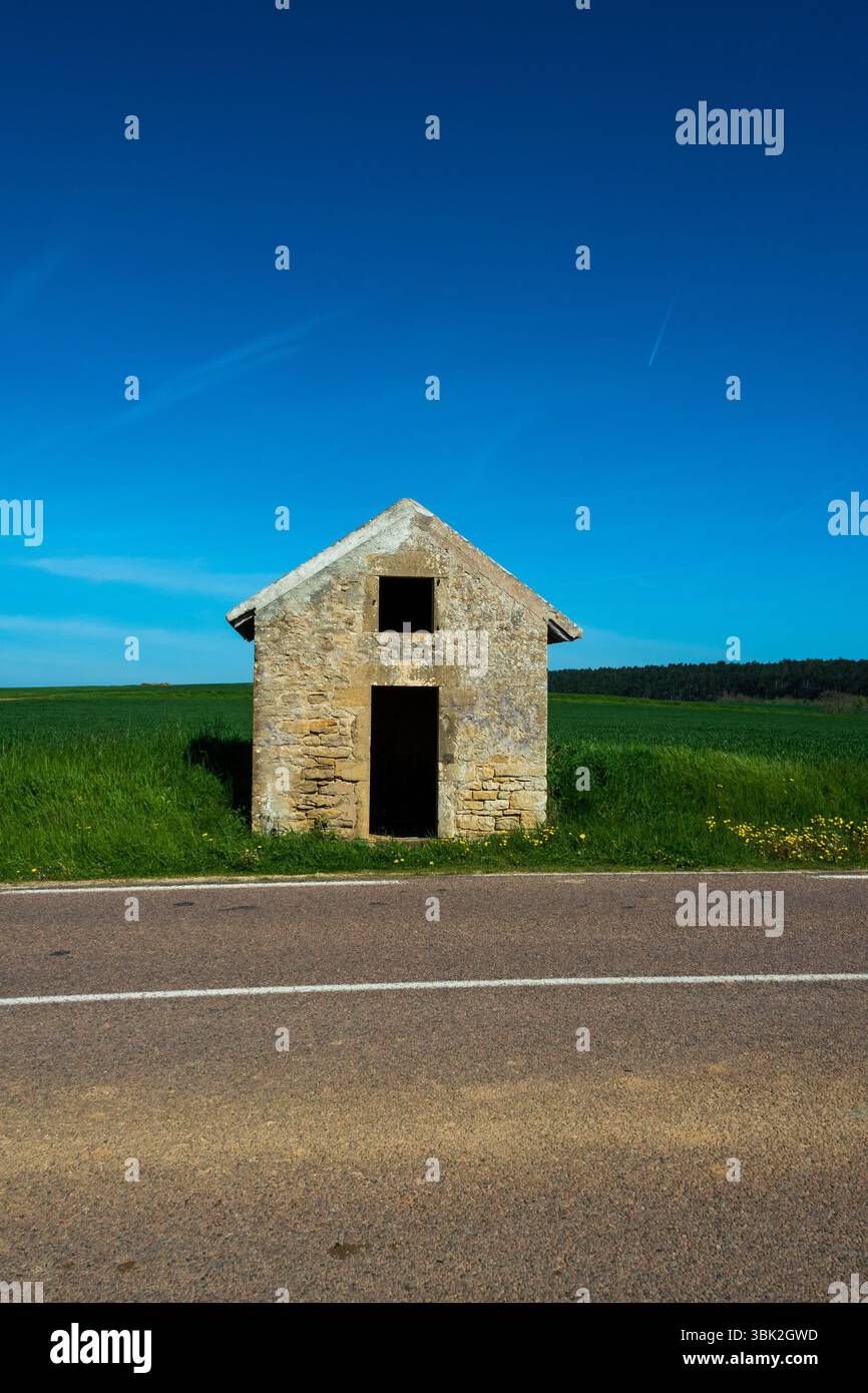 Una rustica capanna di pietra si erge da sola in una strada tranquilla, circondata da vibranti campi verdi. Auvergne. Francia Foto Stock