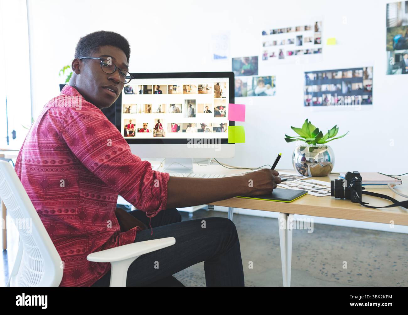 Stilo grafico per tablet che si alza sopra la scrivania in ufficio creativo, con fotocamera reflex digitale e stampe di riferimento Foto Stock