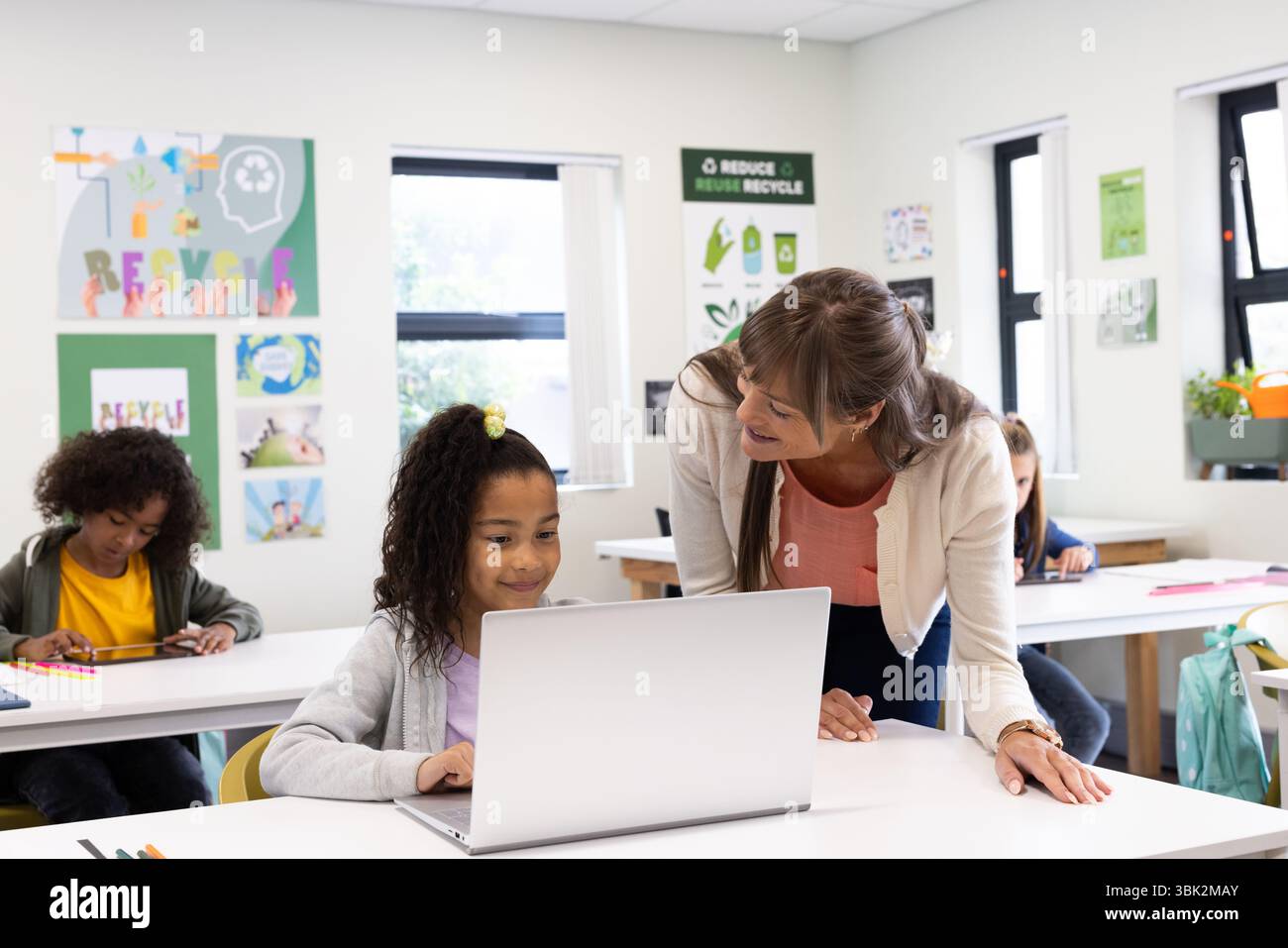 Insegnante di sesso femminile che aiuta una ragazza a utilizzare il notebook in classe, promuovendo l'apprendimento e il coinvolgimento, a scuola Foto Stock