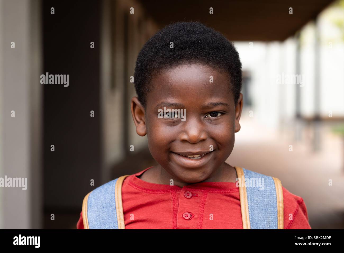 Sorridente ragazzo afroamericano con zaino in piedi nel corridoio della scuola, pronto per la lezione Foto Stock