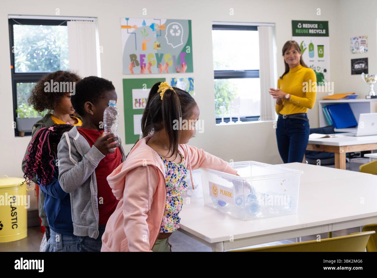 Riciclare bottiglie di plastica, bambini diversi in classe con insegnante femminile che osserva, a scuola Foto Stock