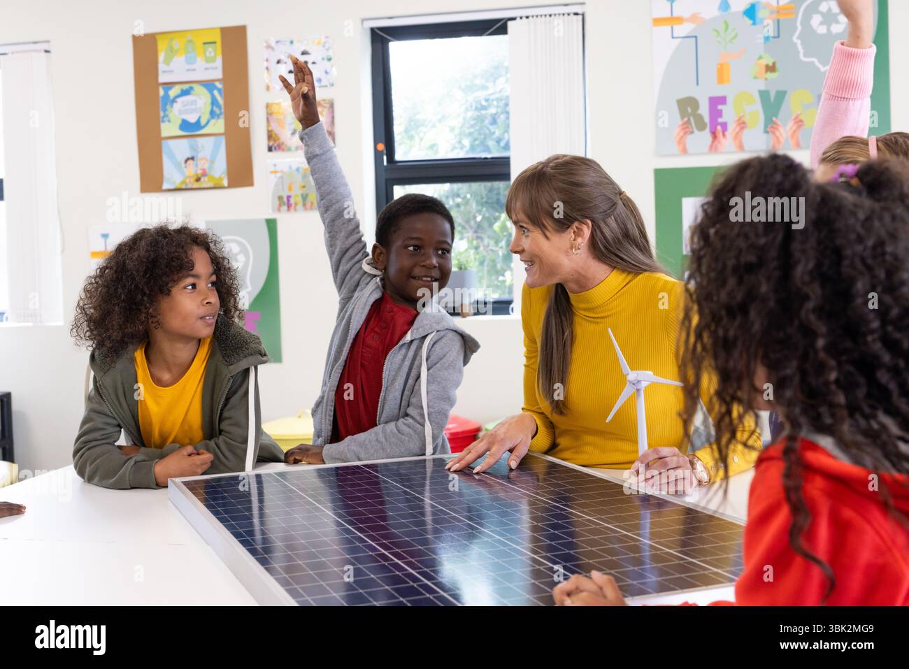 Insegnante femminile che coinvolge diversi studenti sul progetto di energia solare in classe, a scuola Foto Stock