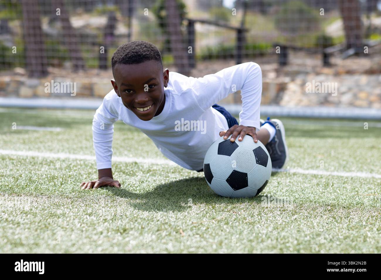 Sorridente ragazzo afroamericano che gioca con il pallone da calcio sul campo, divertendosi all'aperto Foto Stock