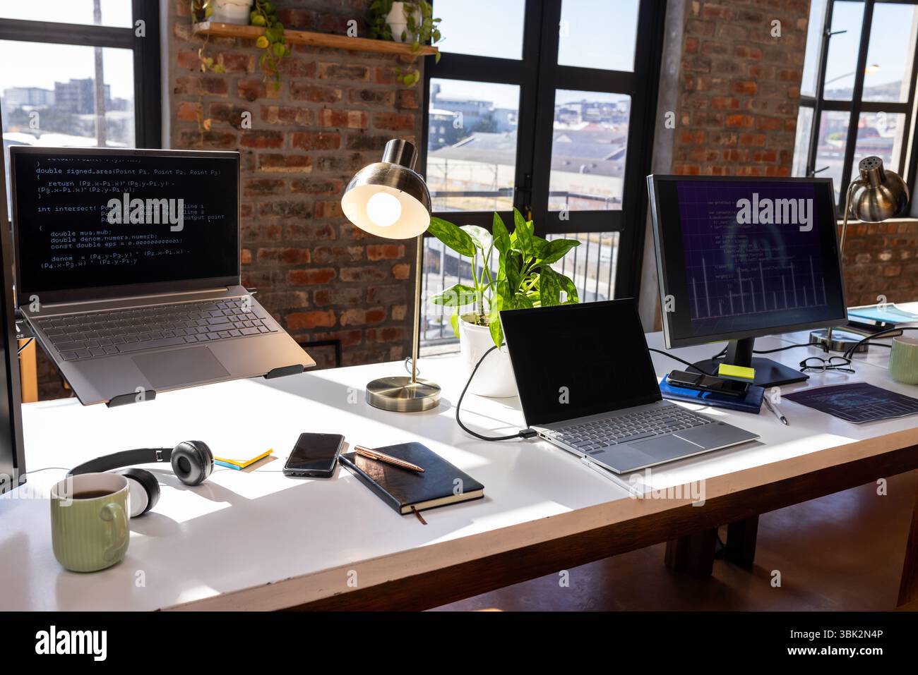 Moderna scrivania da ufficio con computer portatili, codifica su schermo e tazza da caffè Foto Stock