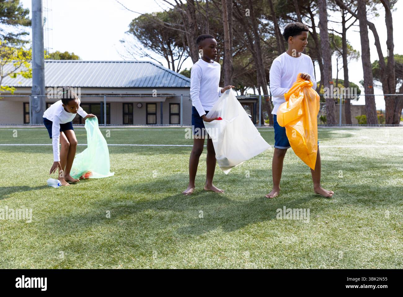 Pulizia del campo scolastico, diversi studenti che raccolgono rifiuti in borse colorate, lavoro di squadra all'aperto Foto Stock