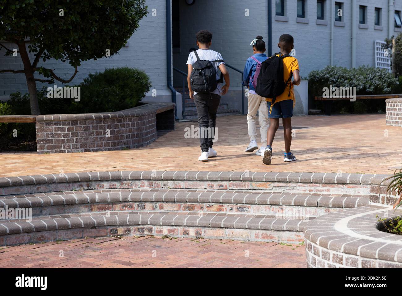 Diversi studenti che camminano fino all'edificio scolastico con gli zaini, godendosi il pomeriggio di sole Foto Stock