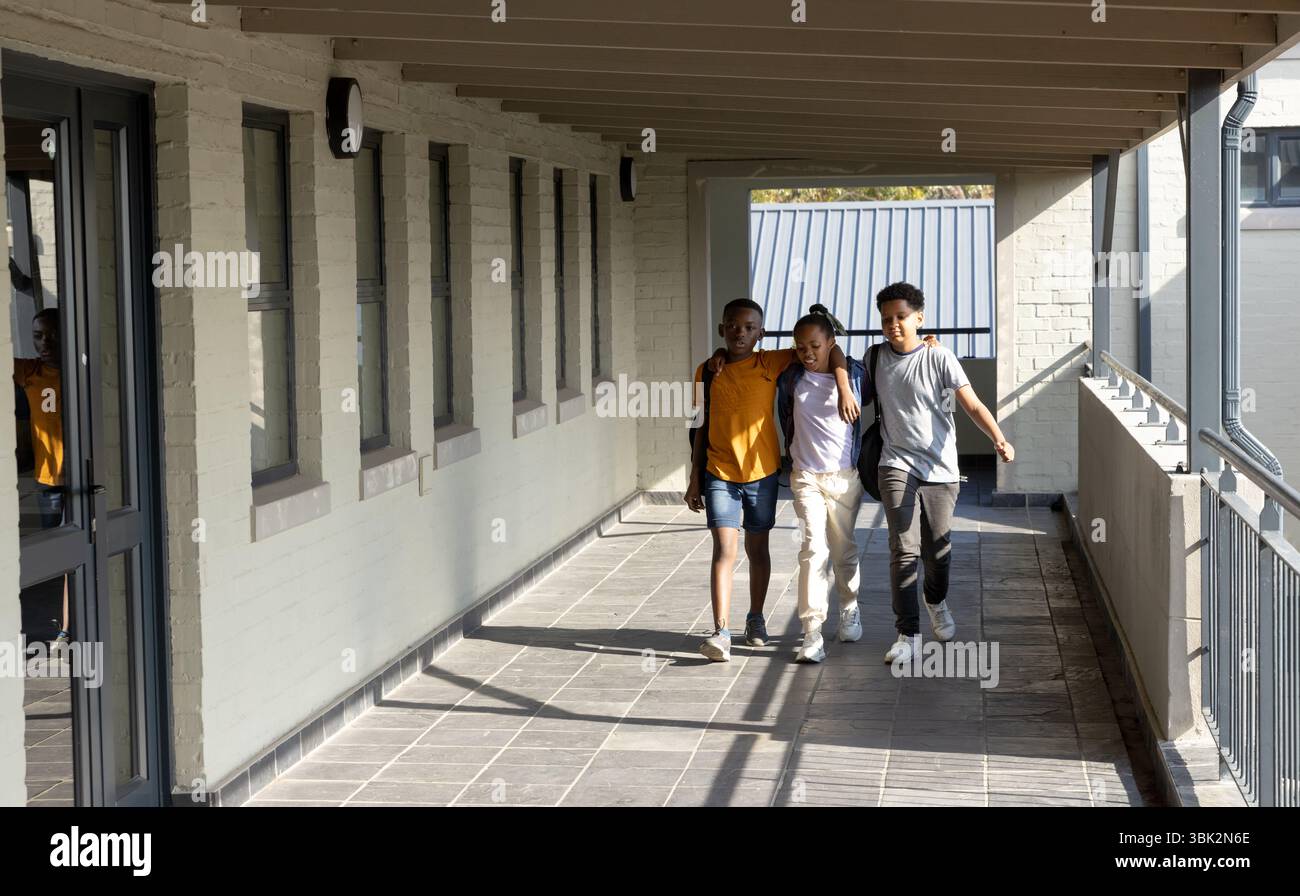 Studenti diversi che camminano insieme nel corridoio della scuola, godendo di amicizia e conversazione Foto Stock
