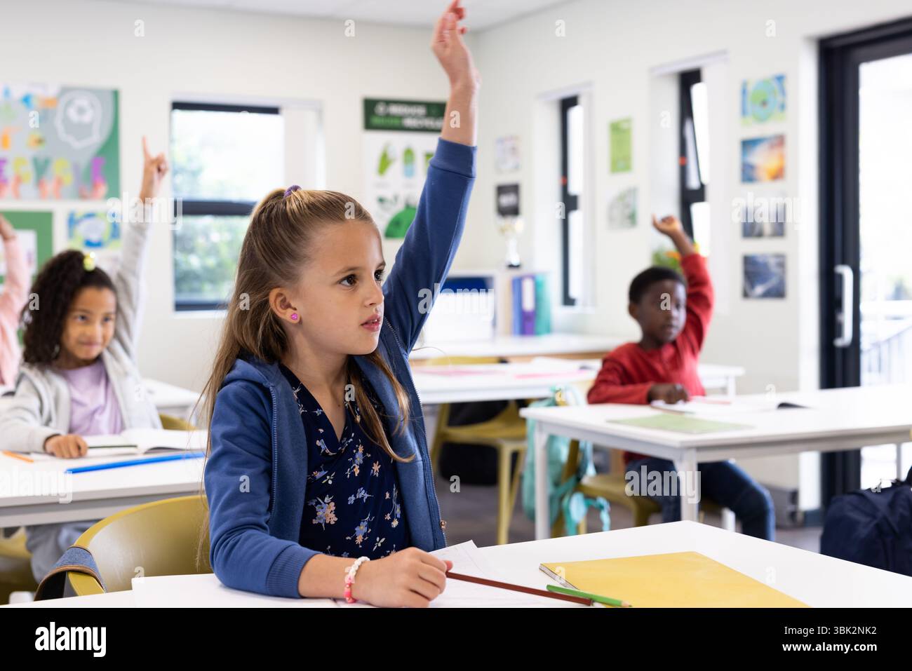 Studenti diversi che alzano la mano in classe, desiderosi di partecipare alle lezioni scolastiche Foto Stock