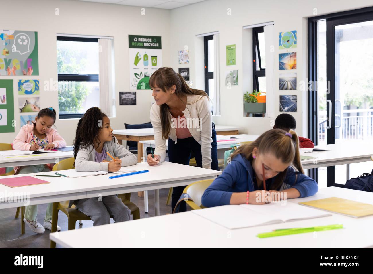 A scuola, insegnante femminile che aiuta studenti diversi con incarichi, promuovendo l'apprendimento Foto Stock