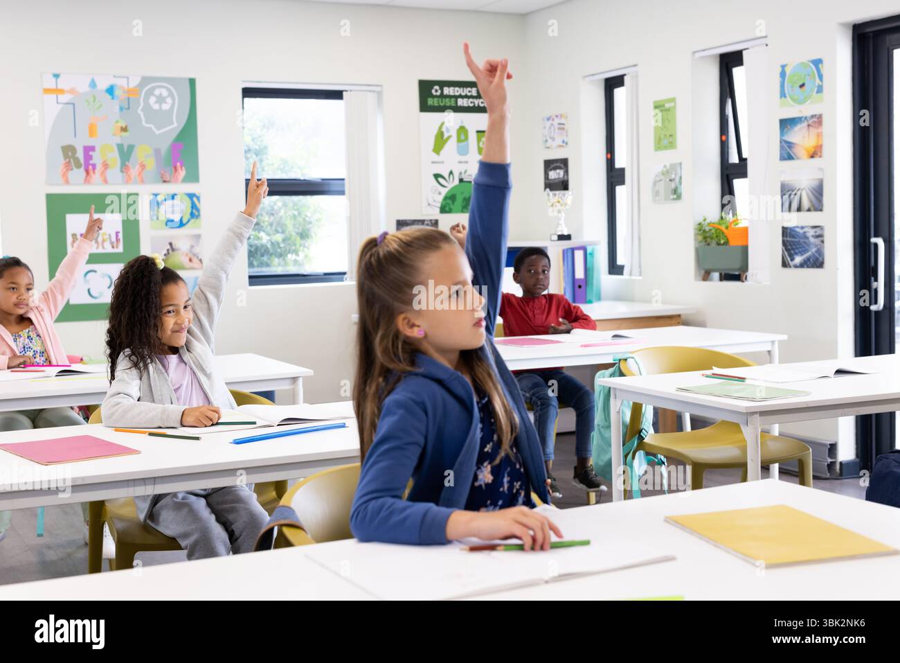 Studenti diversi che alzano con entusiasmo la mano in classe, partecipando a una lezione scolastica Foto Stock