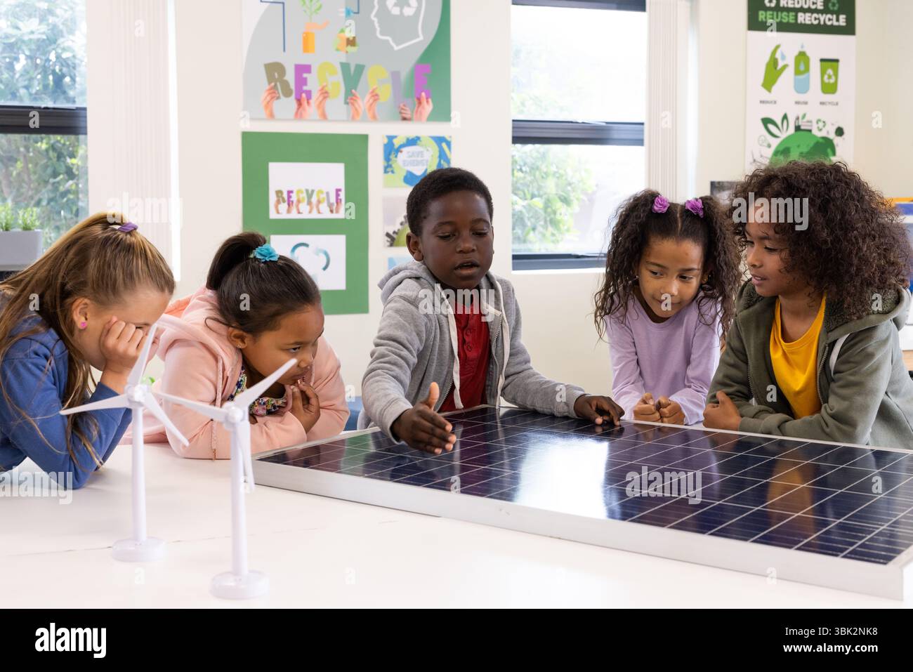 Diversi scolari che esplorano modelli di pannelli solari e turbine eoliche in classe Foto Stock
