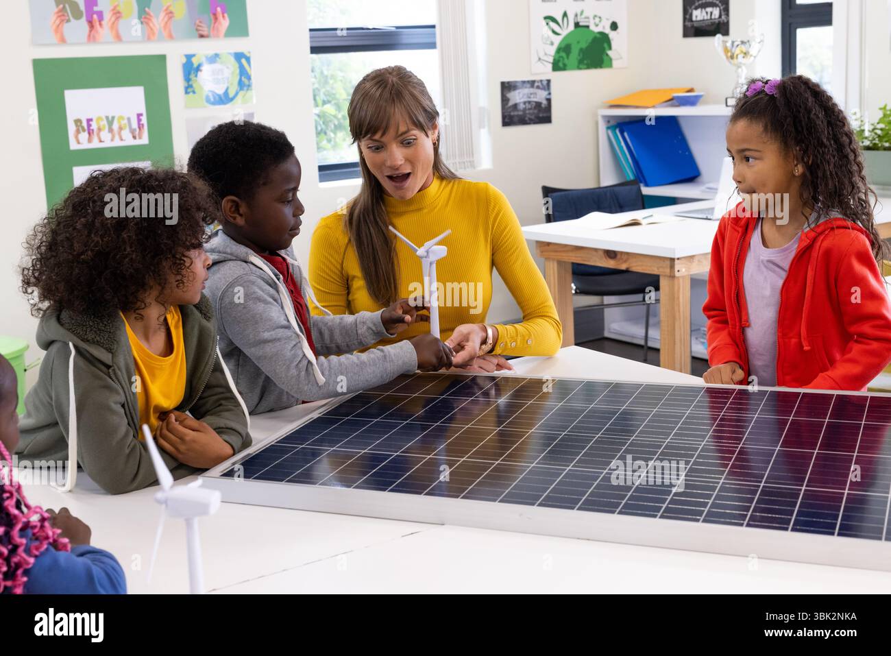 Insegnante femminile e studenti diversi che esplorano l'energia solare con turbine eoliche in classe, a scuola Foto Stock
