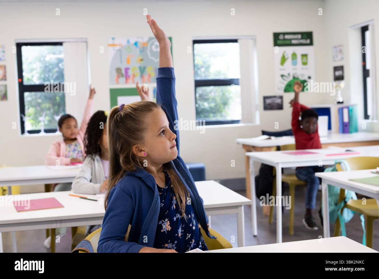 Studenti diversi che alzano la mano in classe, desiderosi di partecipare alle lezioni scolastiche Foto Stock