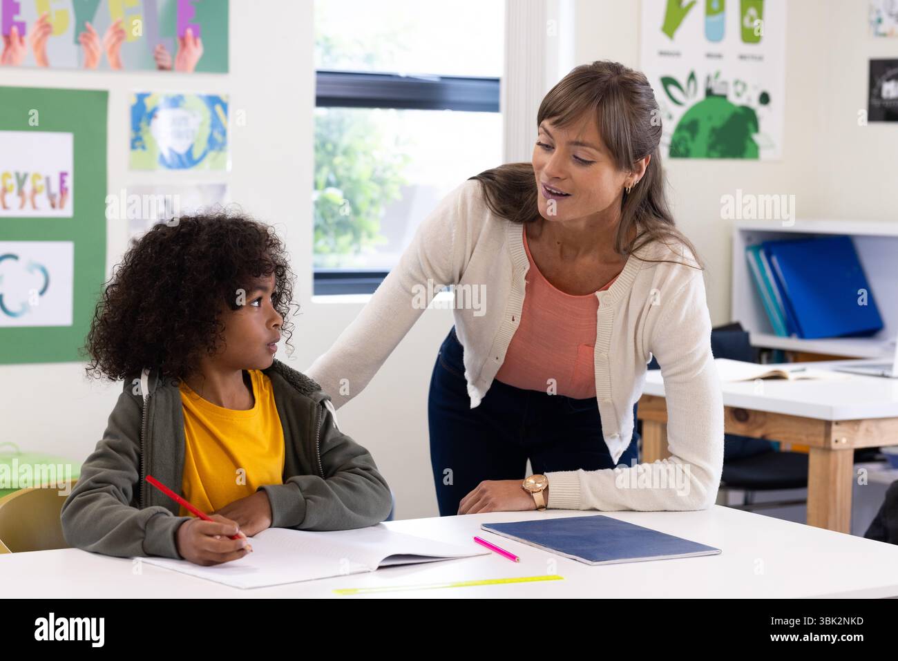 Insegnante donna che aiuta il ragazzo con compiti di scrittura in classe, promuovendo l'apprendimento, a scuola Foto Stock
