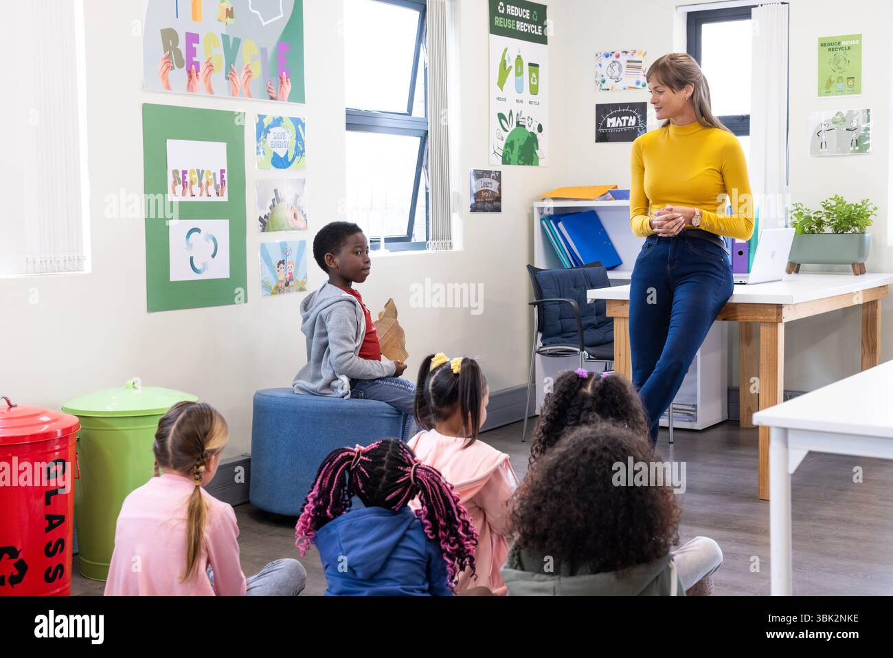 Insegnante femminile che coinvolge studenti diversi in lezioni di riciclaggio in classe, bambini che ascoltano, a scuola Foto Stock