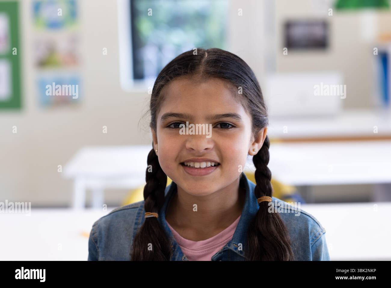 A scuola, ragazza con trecce sorridente, godendo dell'ambiente in classe con i compagni di classe Foto Stock