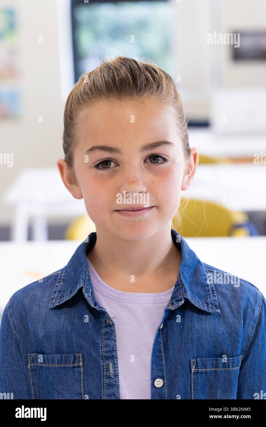 Ragazza sorridente in giacca di denim in piedi con sicurezza in classe luminosa, a scuola Foto Stock
