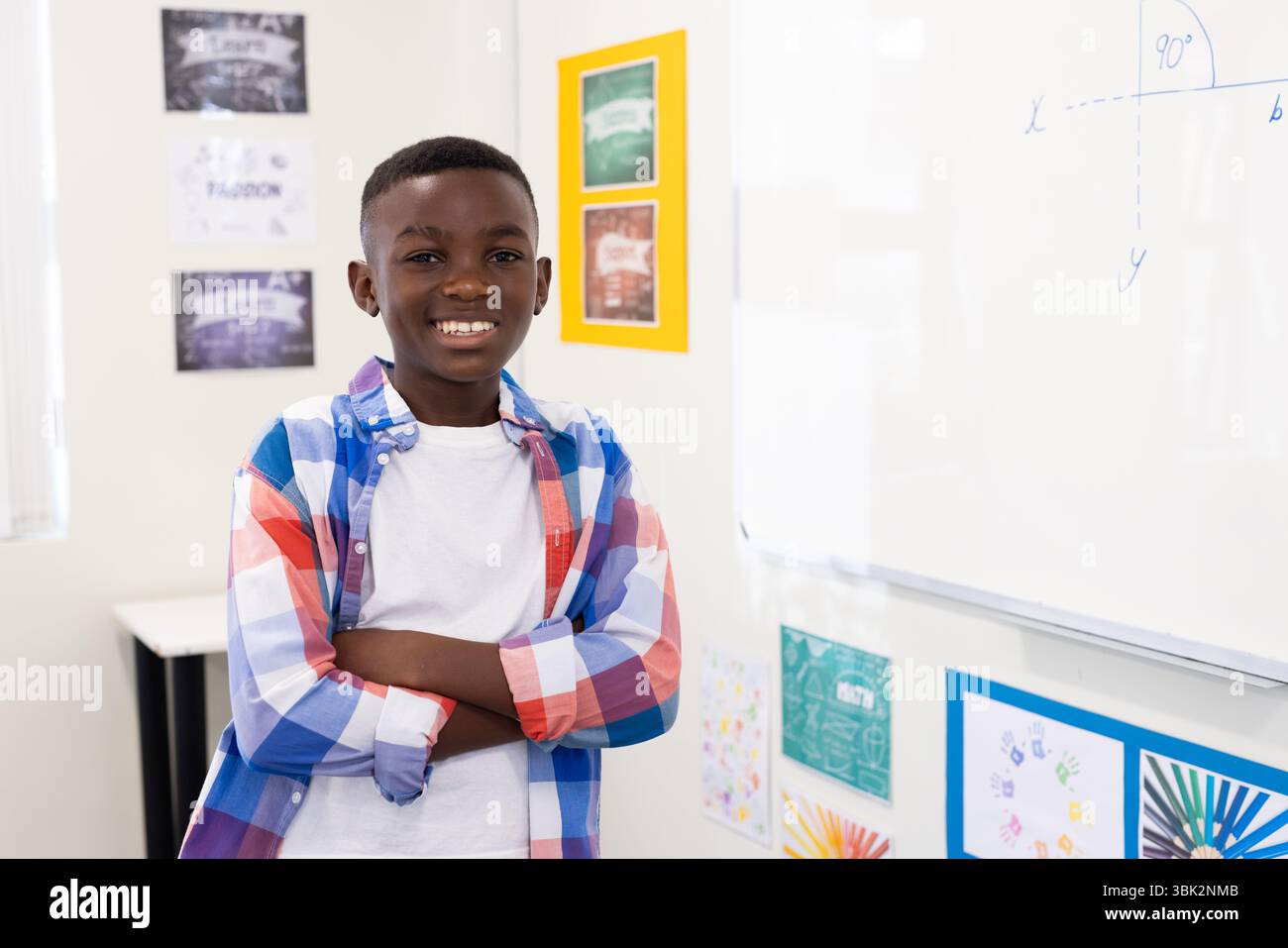 Ragazzo afroamericano che sorride in classe, in piedi sulla lavagna con equazione, a scuola Foto Stock