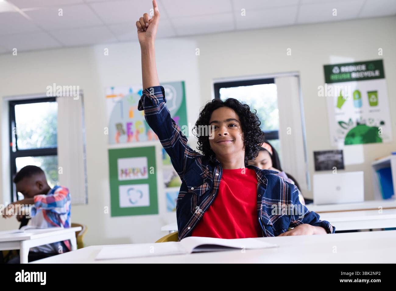 In classe, ragazzo entusiasta che alza la mano, desideroso di partecipare a lezione, a scuola Foto Stock