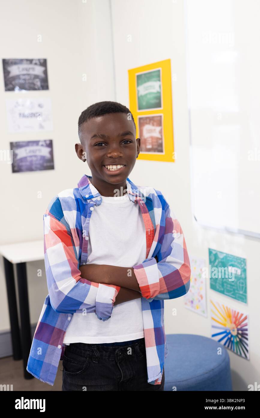 Sorridente ragazzo afroamericano in camicia colorata in piedi in sicurezza in classe a scuola Foto Stock