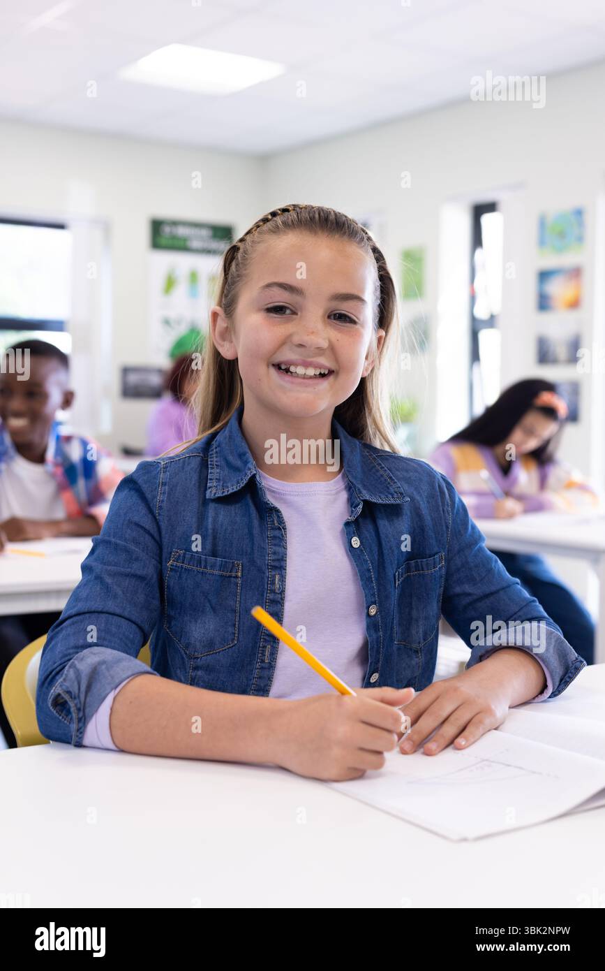 Ragazza sorridente che scrive in classe, che si diverte con i compagni di classe Foto Stock