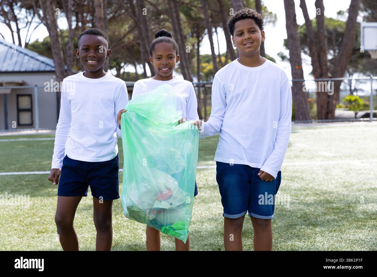 Ripulire il parco giochi della scuola, diversi studenti che tengono in mano il sacco della spazzatura, sorridono e aiutano l'ambiente Foto Stock