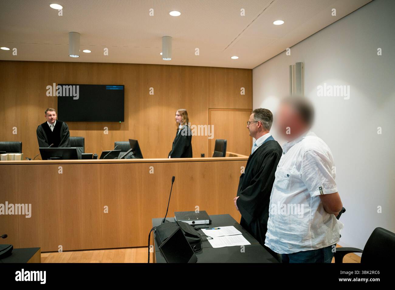 18 giugno 2025, Baviera, Haßfurt: L'imputato (r) e il suo avvocato difensore Marcus Pretzell (2° da destra) si alzano mentre il giudice Keller entra in aula e apre l'udienza nel processo per l'uso di simboli di organizzazioni incostituzionali e terroristiche e l'incitamento del popolo. Nella primavera del 2024, l'accusato avrebbe caricato un file immagine su X con una foto ritratto dell'allora ministro federale dell'economia Habeck (Verdi) e le parole "Schwachkopf PROFESSIONAL". Ciò ha portato a un raid nella casa del sospetto nel distretto di Haßberge nella bassa Franconia. Foto: Daniel Vogl/dp Foto Stock