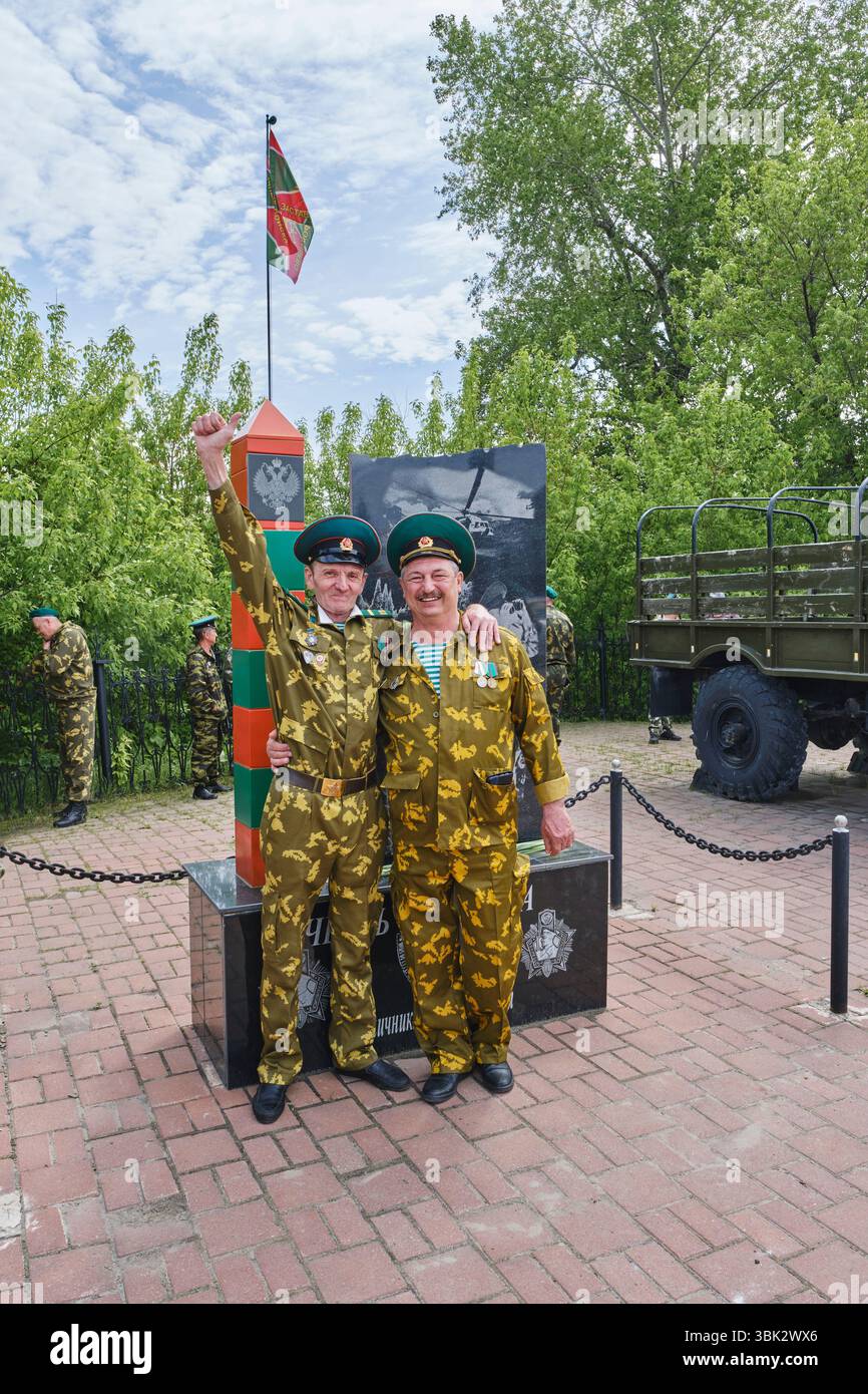 Aromashevo, Russia - 28 maggio 2025: Due veterani in uniforme mimetica si trovano in un memoriale rurale della guardia di frontiera durante la celebrazione del Border Guards Day in R. Foto Stock