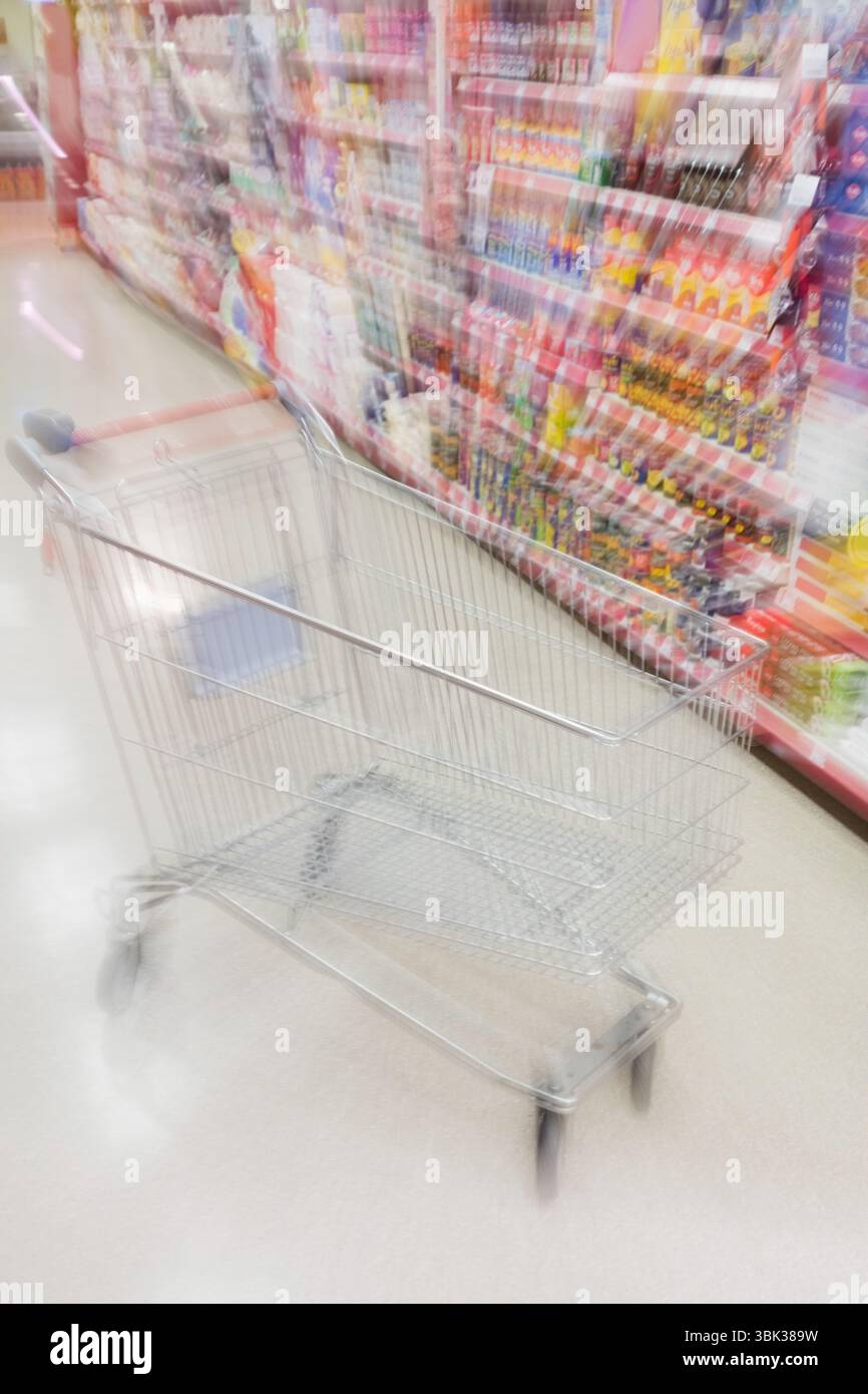 Il carrello della spesa in metallo con manico rosso si sposta lungo il corridoio piatto con scaffali riforniti Foto Stock