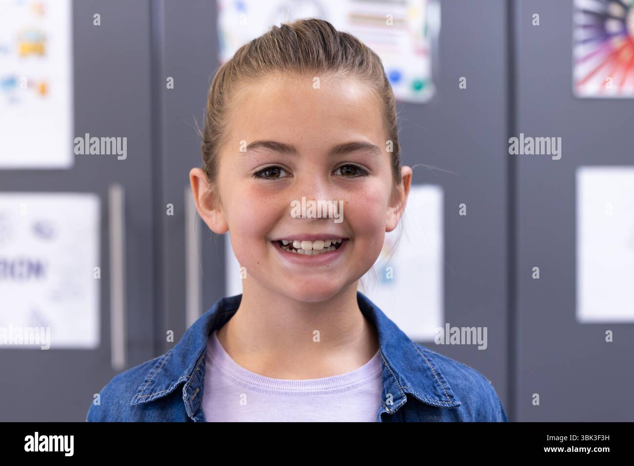 Ragazza sorridente in classe, indossa una giacca in denim e si sente felice a scuola Foto Stock