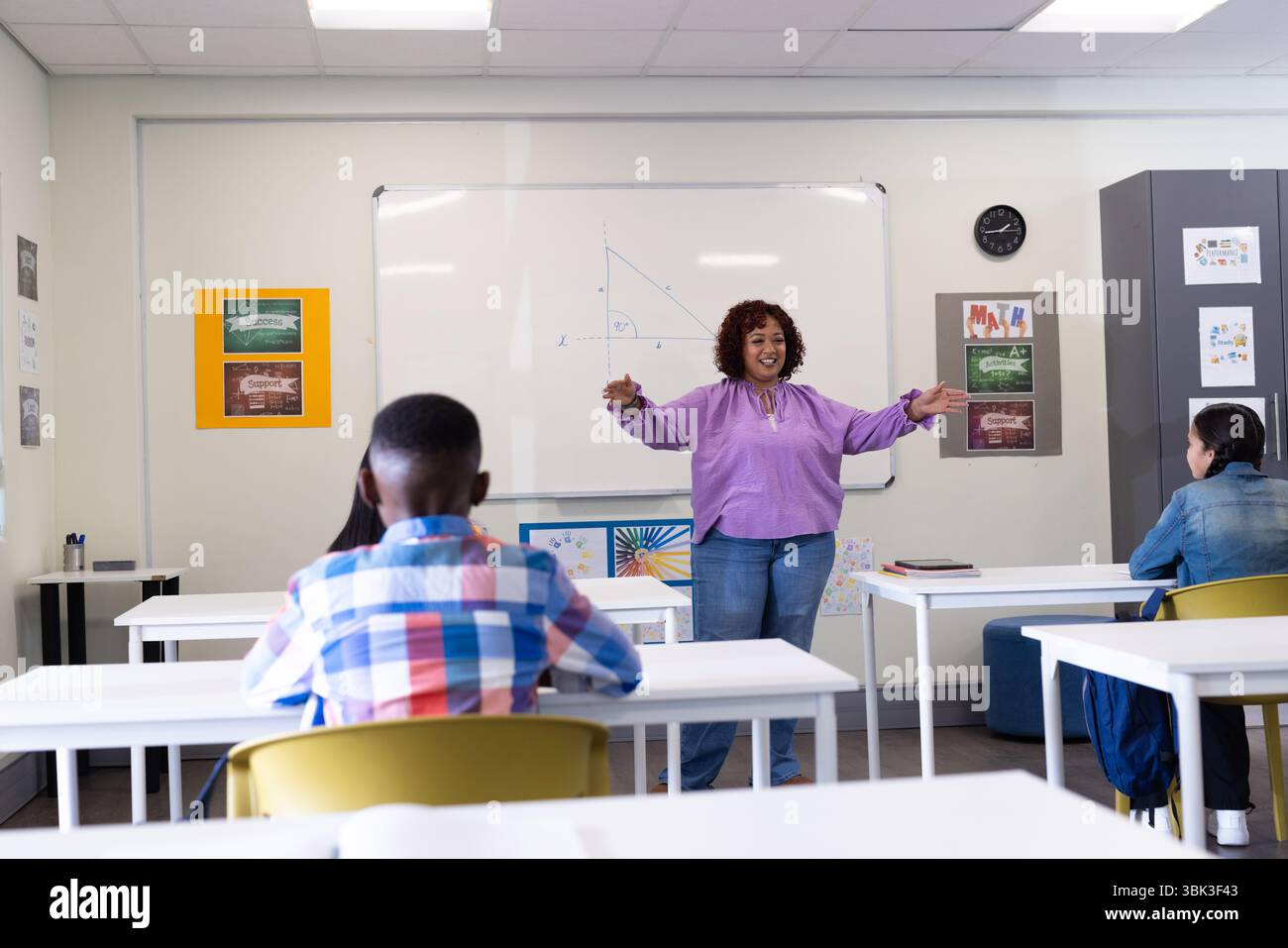 A scuola, insegnante donna che spiega la matematica sulla lavagna, coinvolgendo studenti diversi con entusiasmo Foto Stock