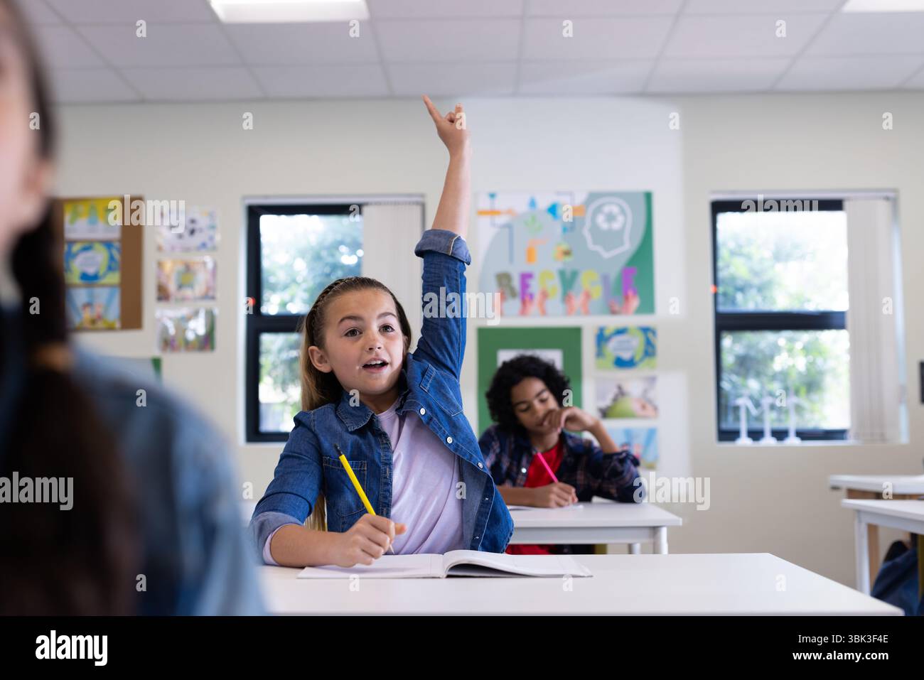 Alzando la mano con la matita, ragazza entusiasta desiderosa di partecipare in classe, a scuola Foto Stock