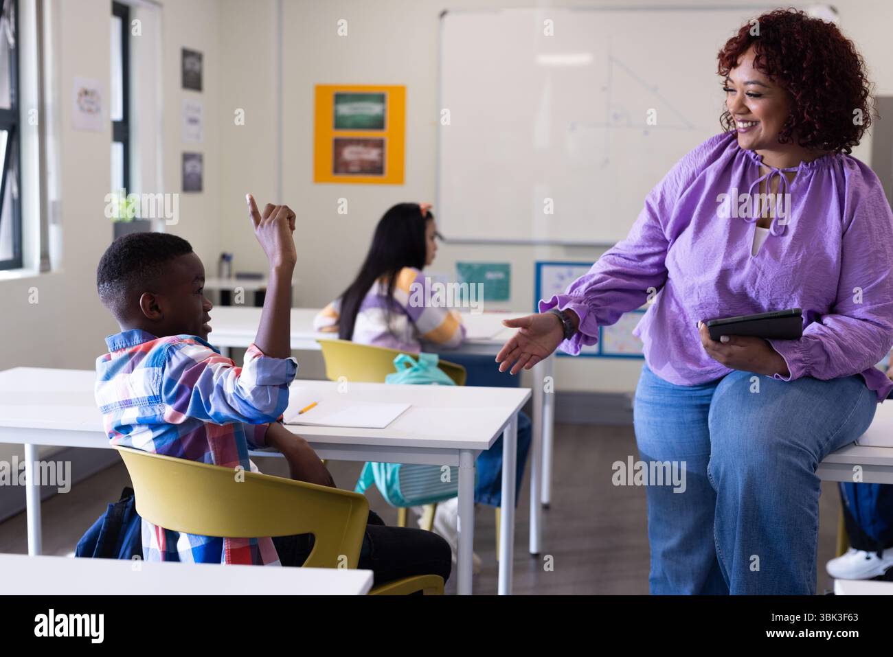 Insegnante femminile che si impegna con la studentessa alzando mano in classe, promuovendo l'apprendimento attivo, a scuola Foto Stock