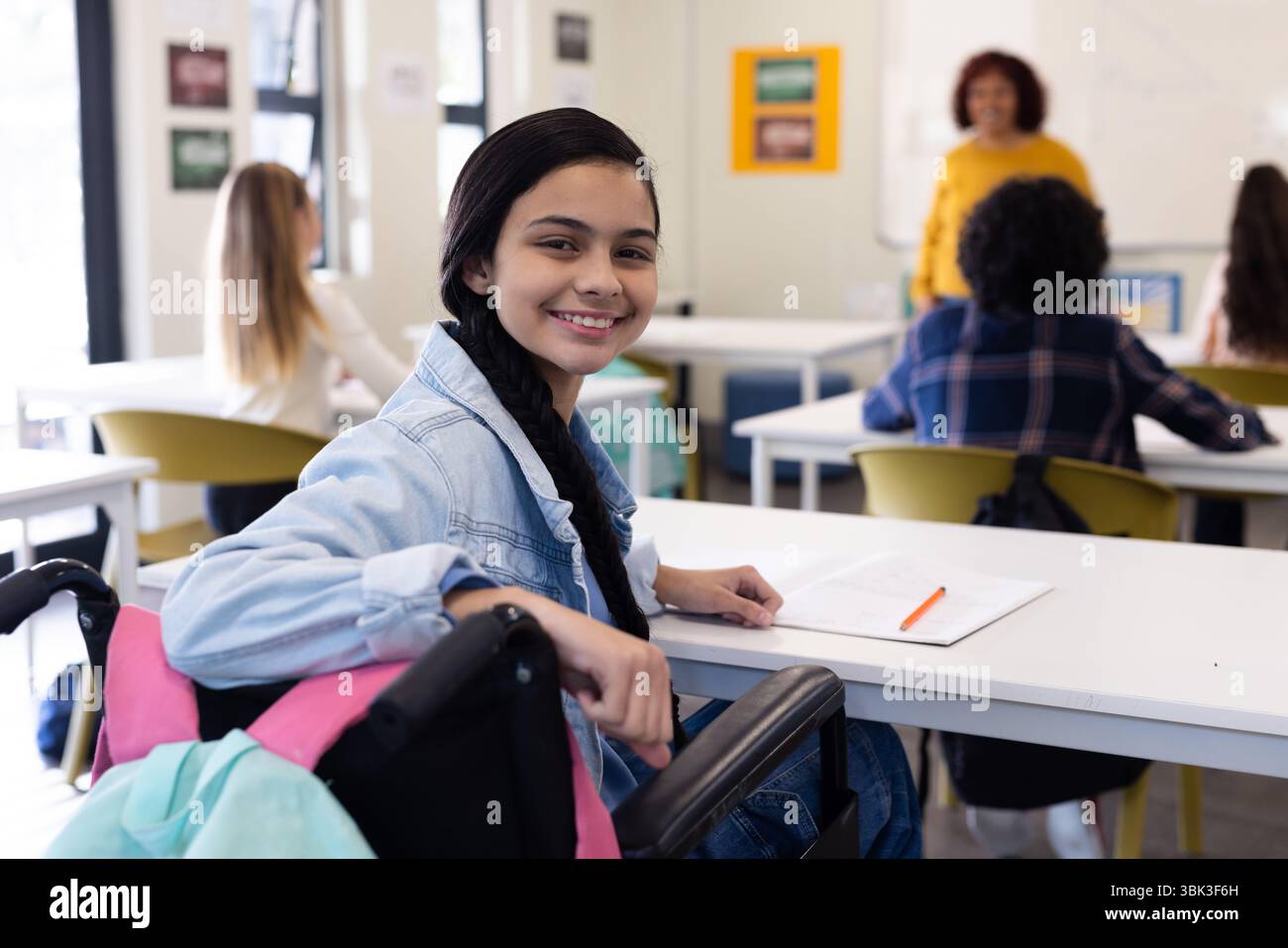 Ragazza sorridente in sedia a rotelle che frequenta la classe scolastica, coinvolgendo un'insegnante femminile Foto Stock