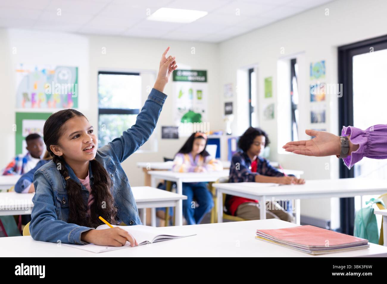 In classe, una ragazza che alza la mano con impazienza mentre un'insegnante con studenti diversi, a scuola Foto Stock