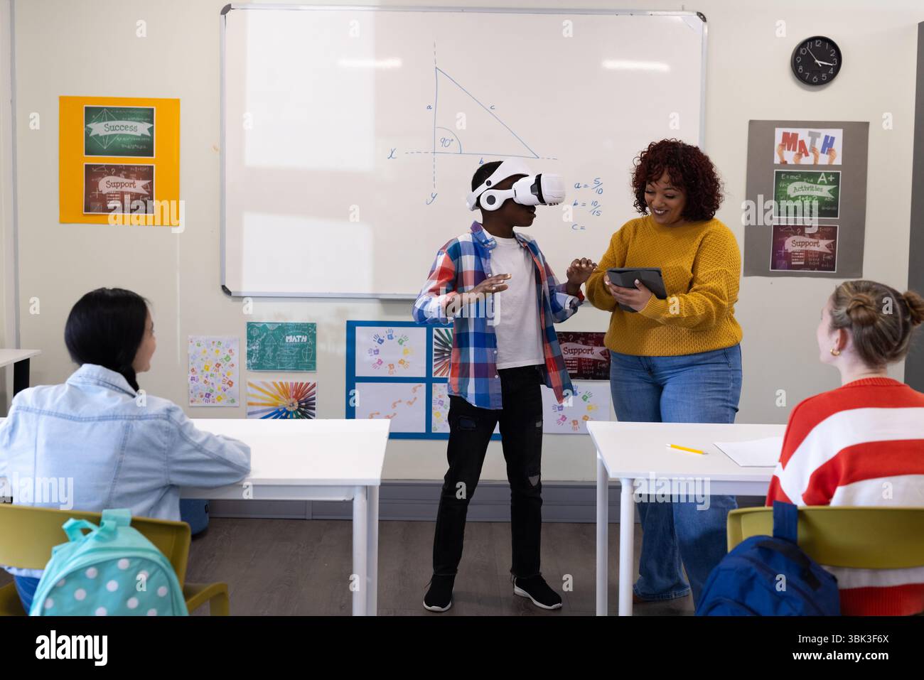 Insegnante donna che guida un ragazzo afroamericano utilizzando il visore vr in classe, a scuola Foto Stock
